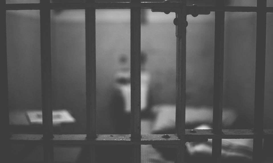Gefängniszelle mit Gitterstäben im Vordergrund als schwarz weiß Bild